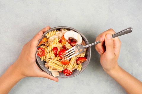 Eating a pasta salad with sliced mushroom, tomato, red pepper pieces and tuna, healthy food with