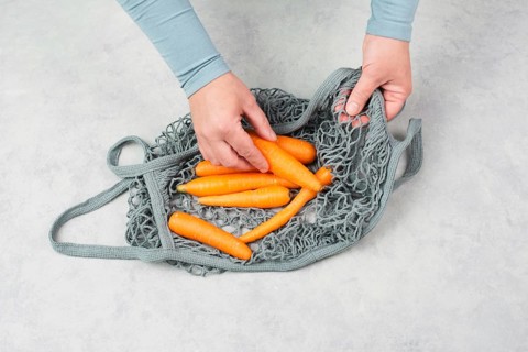 Unpack fresh carrots from a reusable grocery mesh bag, vegetables from the market, healthy food and