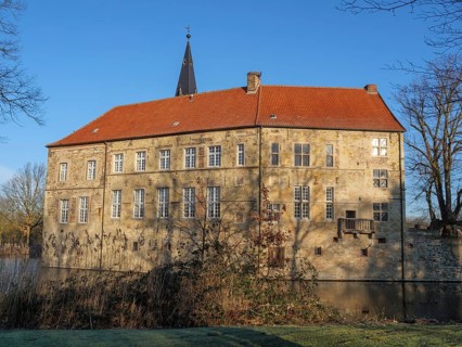 An old moated castle with a red roof, surrounded by water and trees under a blue sky, lüdinghausen,