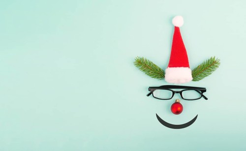 Face of a reindeer with a red bauble nose, fir antlers, a santa claus hat and eyeglasses, merry