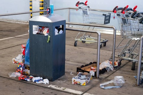 Overflowing dumpster, trash can with plastic bags and cardboard, filthy shopping center,