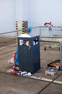 Overflowing dumpster, trash can with plastic bags and cardboard, filthy shopping center,