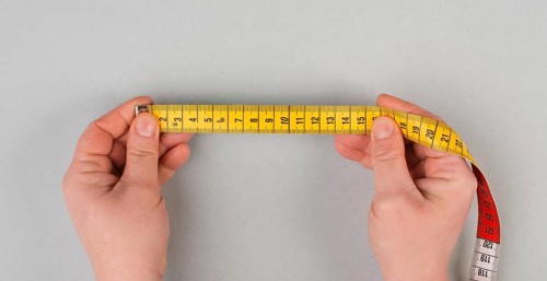 Hand holding yellow tape measure, fitness and diet concept, control with measurement