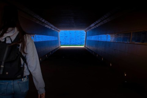 A woman in a dark tunnel walks towards a bright blue exit labelled Waterland, Ilpendam, Netherlands
