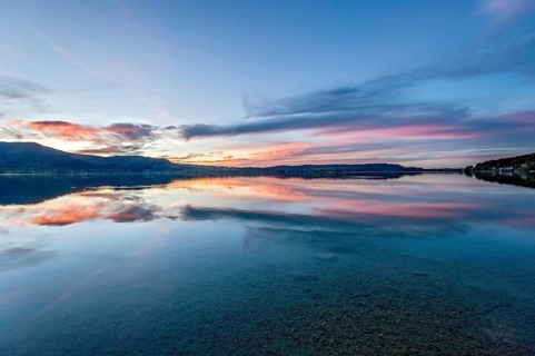 Lake Kochel with reflection of sun and clouds at sunset, calm water, in the background the