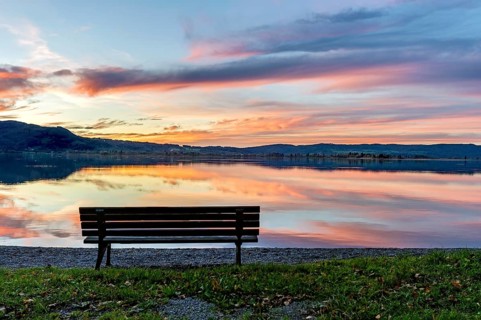 Bench at Lake Kochel, reflection of sun and clouds at sunset, calm water, Kochel am See, Bavarian
