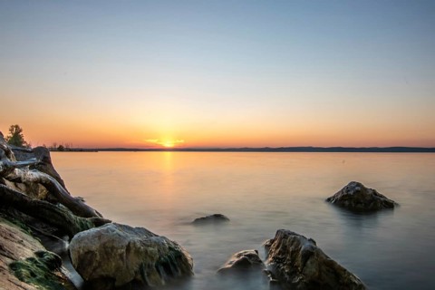 Sunset on the shore of a lake in summer. Colourful sky with a wide view of the horizon. Natural
