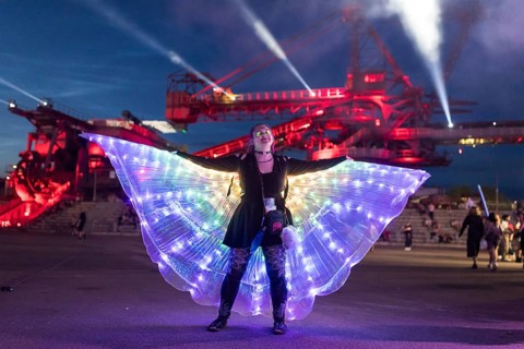 Festival visitor with a bright dress dances in front of an excavator at the Melt Festival in