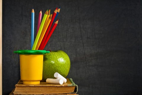 Multicolor pencil, chalk and green apple on old textbook against blackboard in class. School