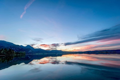 Lake Kochel with reflection of sun and clouds at sunset, calm water, in the background the