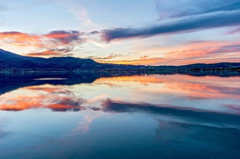 Lake Kochel with reflection of sun and clouds at sunset, calm water, in the background the