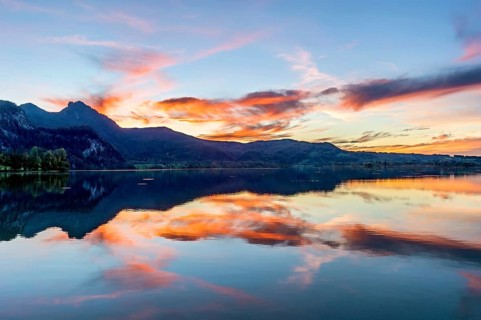 Lake Kochel with reflection of sun and clouds at sunset, calm water, behind the mountains Stein,