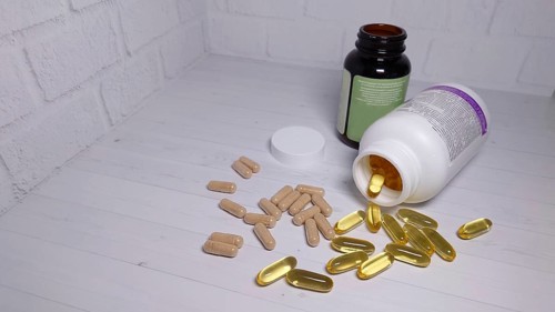 Scattered pills and capsules near two bottles on a white table against a brick wall