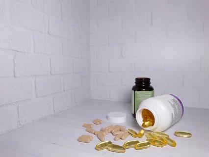 Two bottles of vitamins with spilled pills on a white surface against a white brick wall