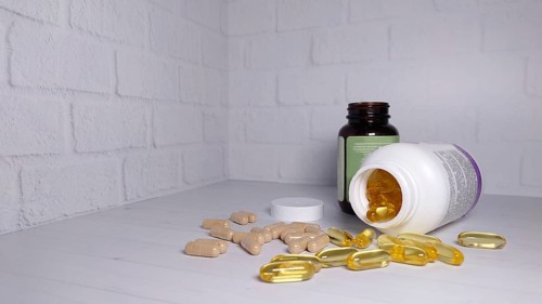 Supplements and pills scattered on a white surface with two bottles, one transparent and one