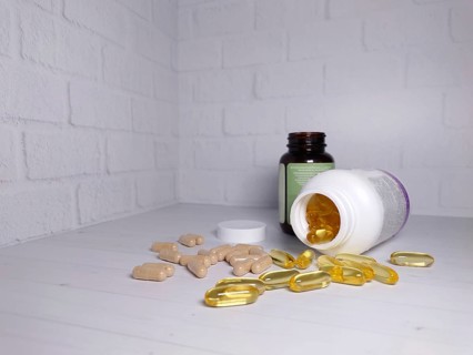 Opened supplement bottles with scattered pills and capsules on a white brick wall background