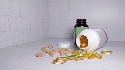 Vitamin and supplement capsules spilled on a white table with brown and white pill bottles