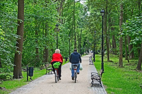 Two cyclists on a narrow road with benches through a forest in Swinoujscie, Swinemünde, West