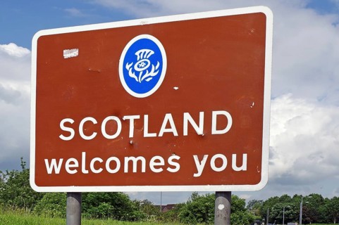 Brown sign with the inscription 'Scotland welcomes you' against a background of trees and cloudy
