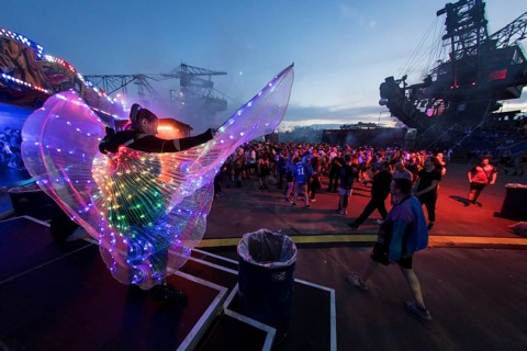 Festival visitor with a bright dress between excavators in the evening at the Melt Festival in