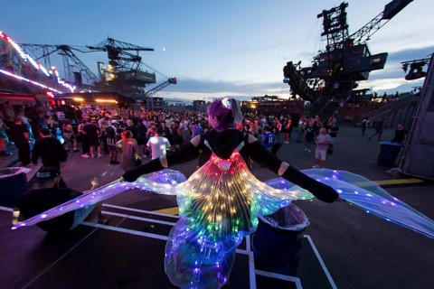 Festival visitor with a bright dress between excavators in the evening at the Melt Festival in