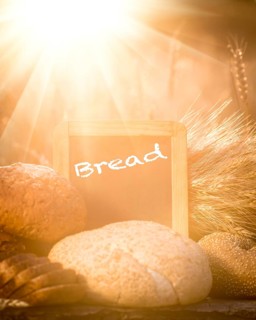 Bread and wheat on the wooden table in autumn field. Blackboard with copyspace