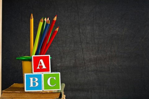 ABC and multicolored pencil on old textbook against blackboard in class. School concept
