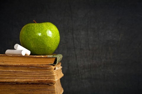 Chalk and green apple on old textbook against blackboard in class. School concept