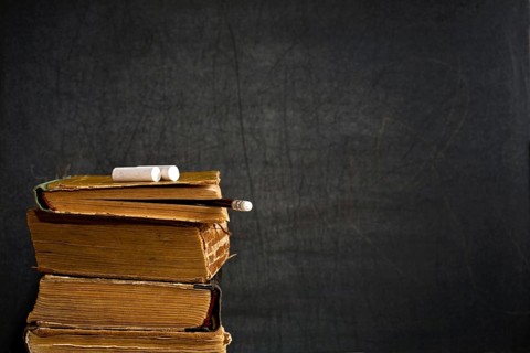 Chalk and pencil on old textbook against blackboard in class. School concept