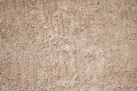A close-up of a beige stucco wall with a rough textured surface