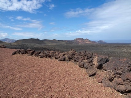 Large desert landscape with reddish soil and black lava rock in the foreground under a blue sky,