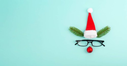 Face of a reindeer with a red bauble nose, fir antlers, a santa claus hat and eyeglasses, merry