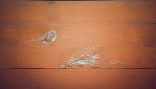A close-up of orange-brown wooden planks with a noticeable knot and scratches, showcasing a rustic