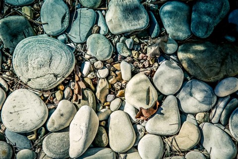 A collection of various sized rocks and pebbles on the ground with sunlight and shadows, and an