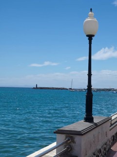 Coastal view of the calm sea with a lantern in the foreground and a harbour in the background under