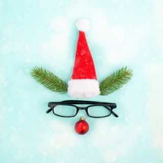 Face of a reindeer with a red bauble nose, fir antlers, a santa claus hat and eyeglasses, merry