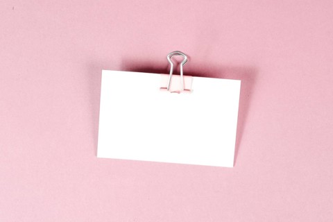 Blank white paper with a paperclip on a pink colored background, copy space for text, reminder or