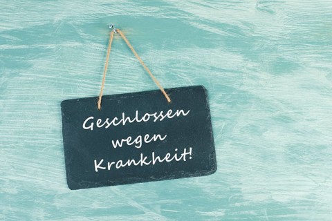 The words closed because of illness are standing in german language on a chalkboard sign, hanging