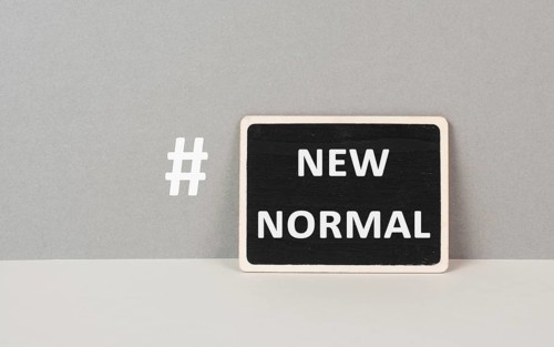 The words new normal with a hashtag are standing on a chalkboard, gray colored background