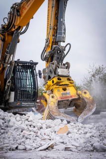 Yellow demolition excavator with grab crushes rubble on a construction site, a large amount of