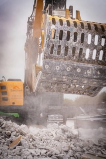 Demolition excavator with a metal grab crushes concrete rubble, raises dust on a construction site,