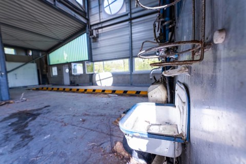 Abandoned hall with metal walls and an old washbasin in the foreground, demolition site,