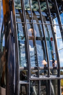 A driver in a construction vehicle, seen through the window with reflections and bars, demolition