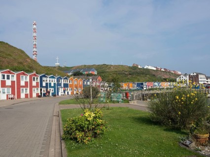 Colourful houses and a lighthouse on a quiet street next to a meadow, Heligoland, North Sea,
