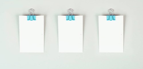 Blank white papers with a paperclip on a gray colored background, copy space for text, reminder or