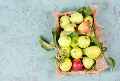 Basket with fresh ripe apples standing on a table, fruit harvest in the summer, healthy organic