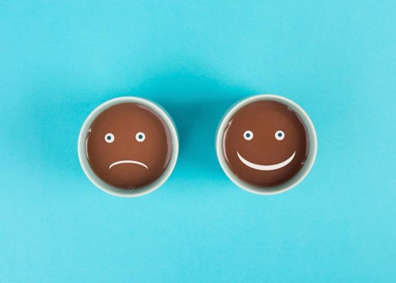 Cup of coffee with a sad and a happy face, positive and negative mindset, support and evaluation