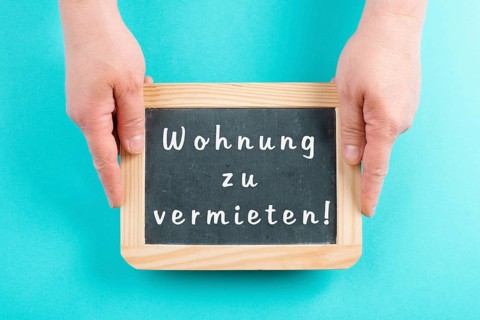 Holding a chalkboard in the hands, apartment for rent is standing in german language on the sign,