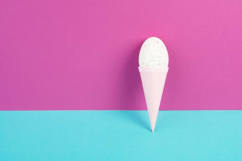 Ice cream cone with an egg, pink and blue background, copy space, easter holiday, summer season,