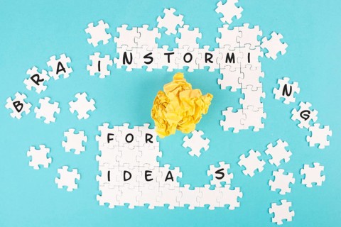 Puzzle on a blue background, yellow crumpled paper, words brainstorming for ideas are standing on